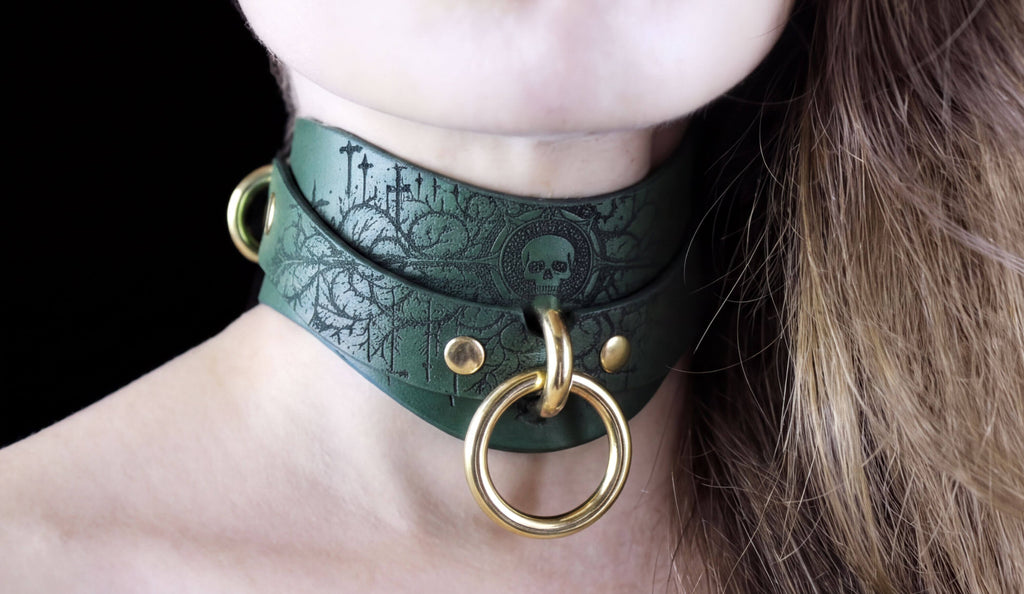 A close-up of a person's neck wearing a green leather choker necklace with a skull design and gold-colored metal rings.