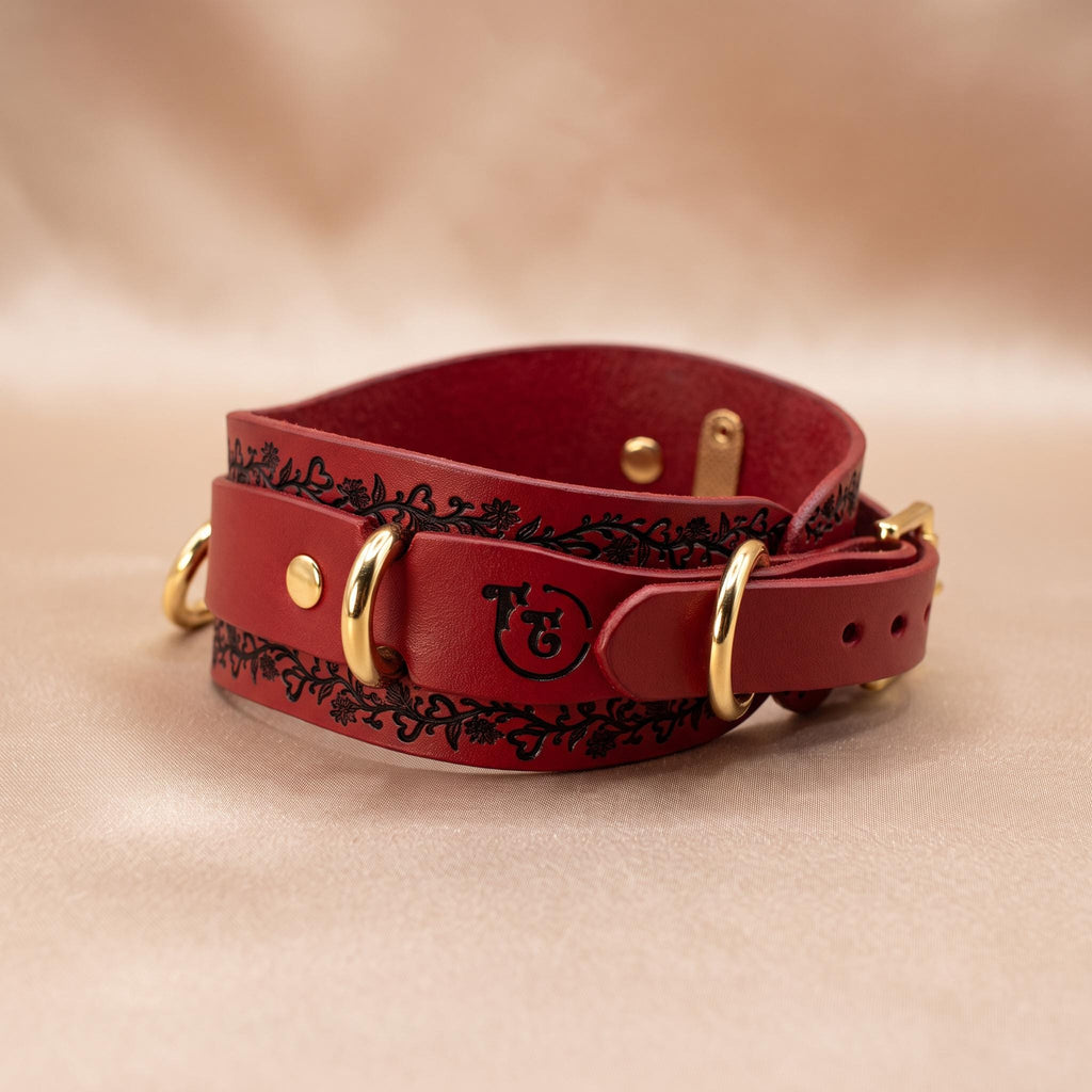 A red leather collar with a floral pattern and gold hardware.