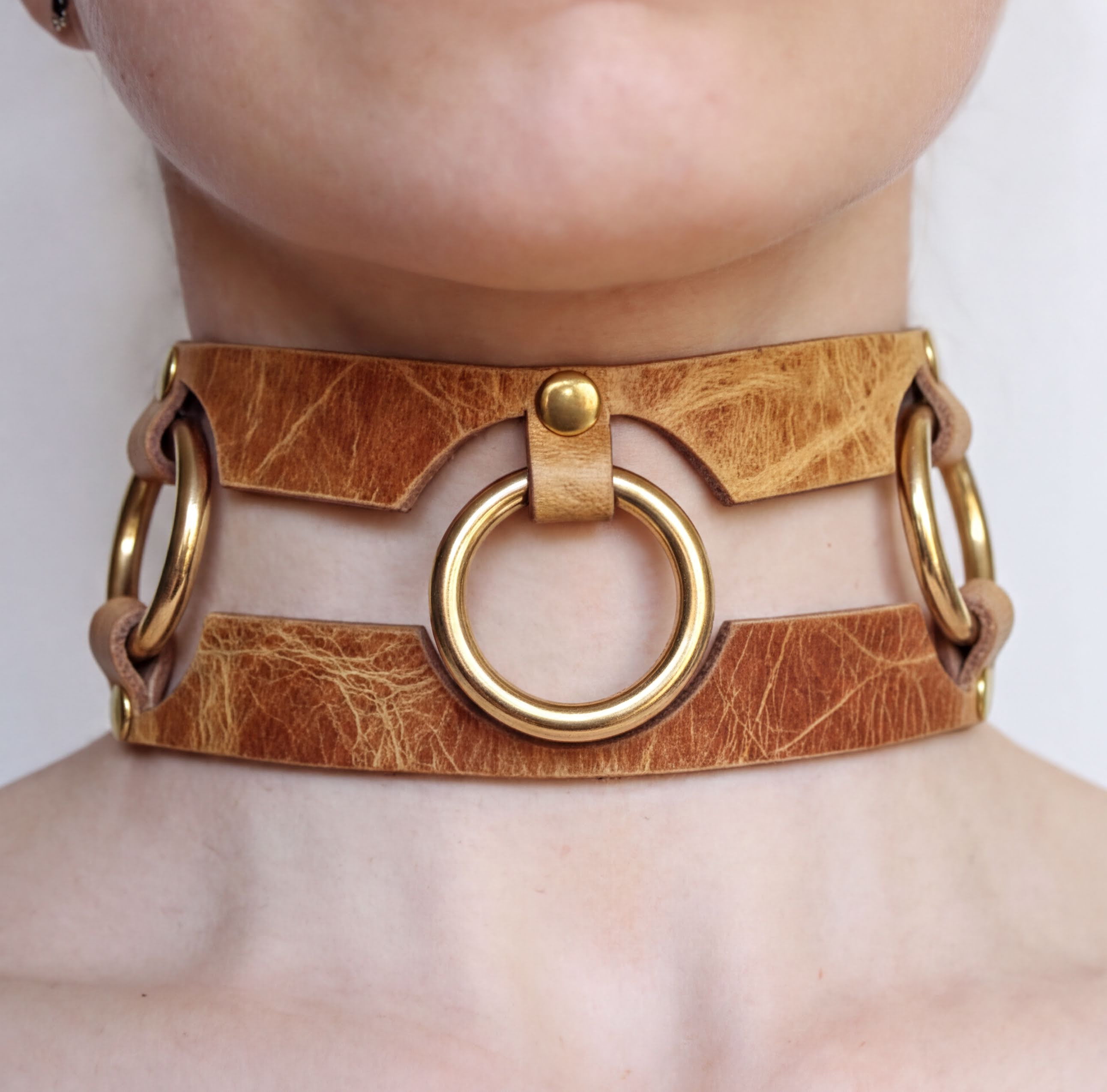 A close-up of a person's neck wearing a choker-style leather necklace with gold-colored metal rings.