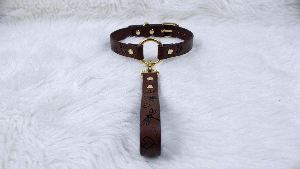 A brown leather collar with a gold buckle and handle is displayed on a white furry surface.