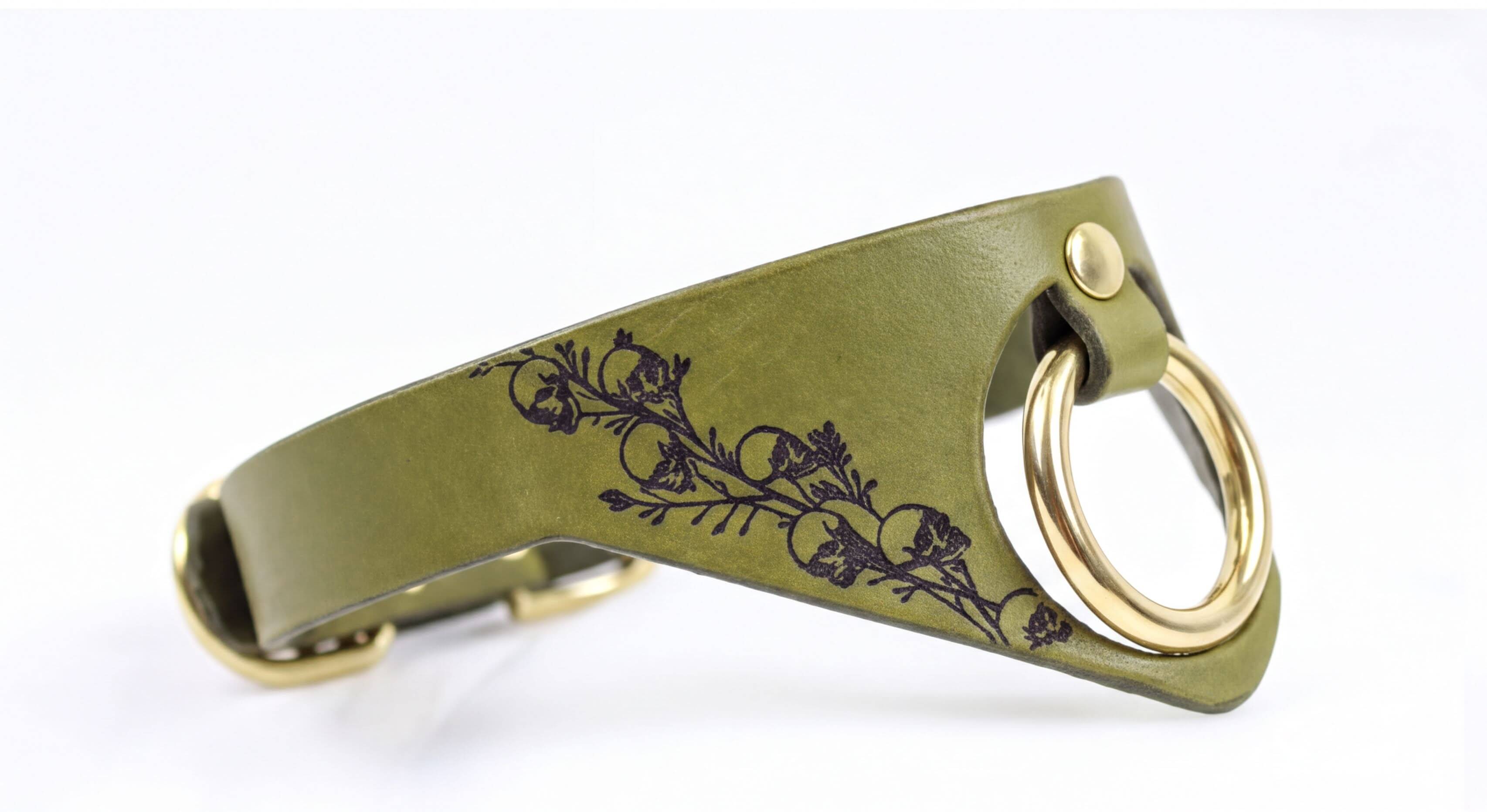 A green leather collar with a gold-colored metal ring and a floral design on the side.