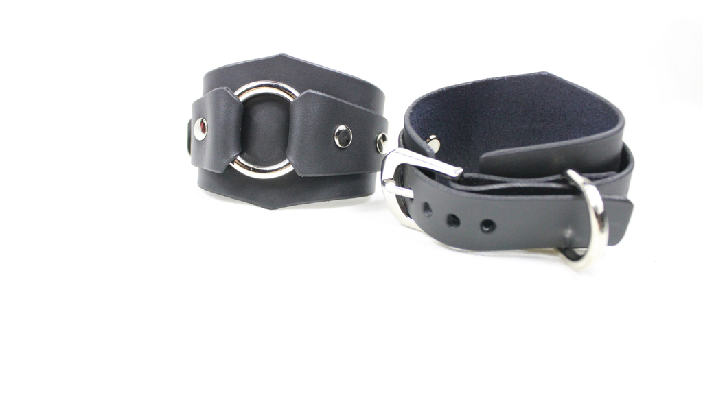 A pair of black leather cuffs with metal buckles and straps, placed side by side on a white background.