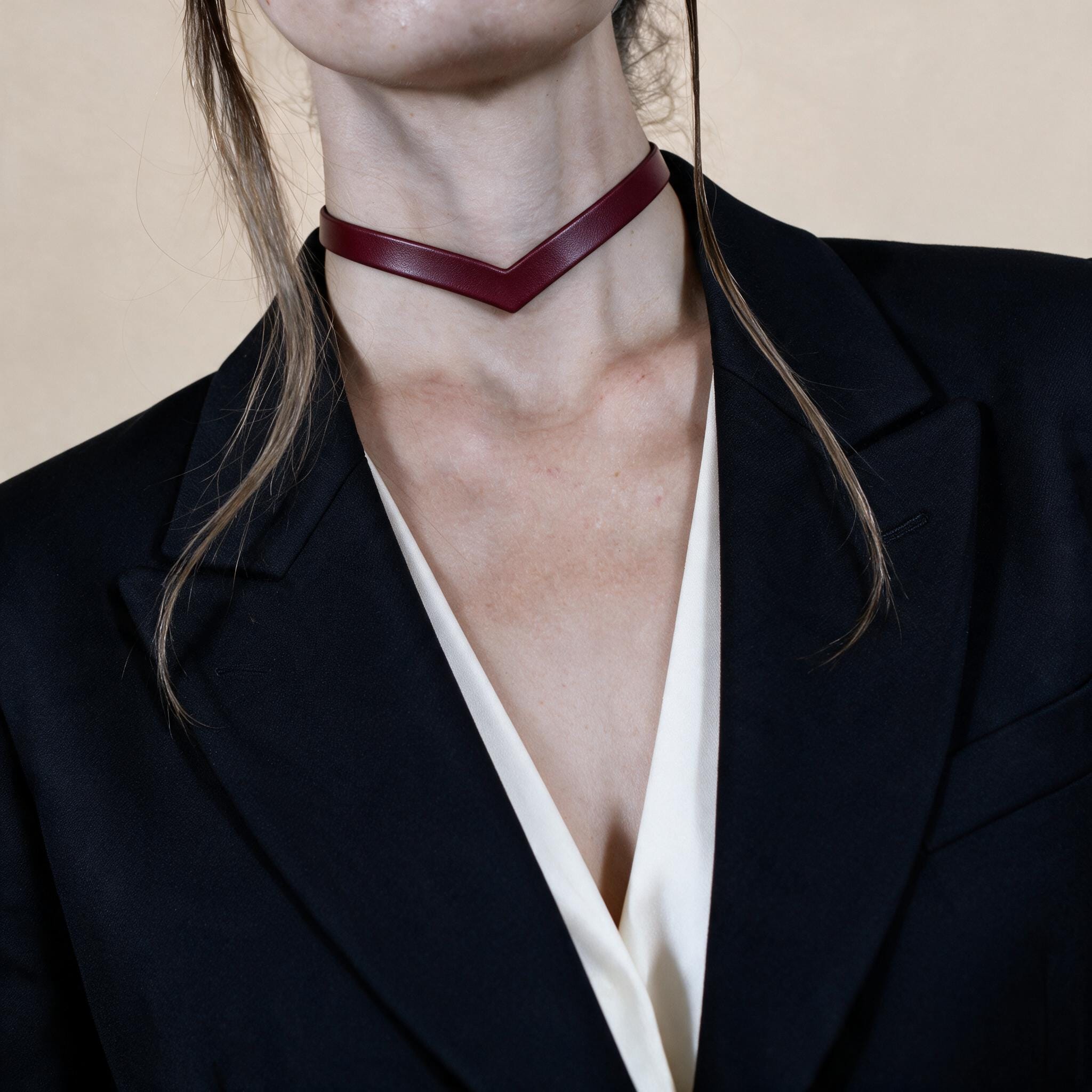 A close-up of a woman wearing a burgundy choker necklace and a black blazer.