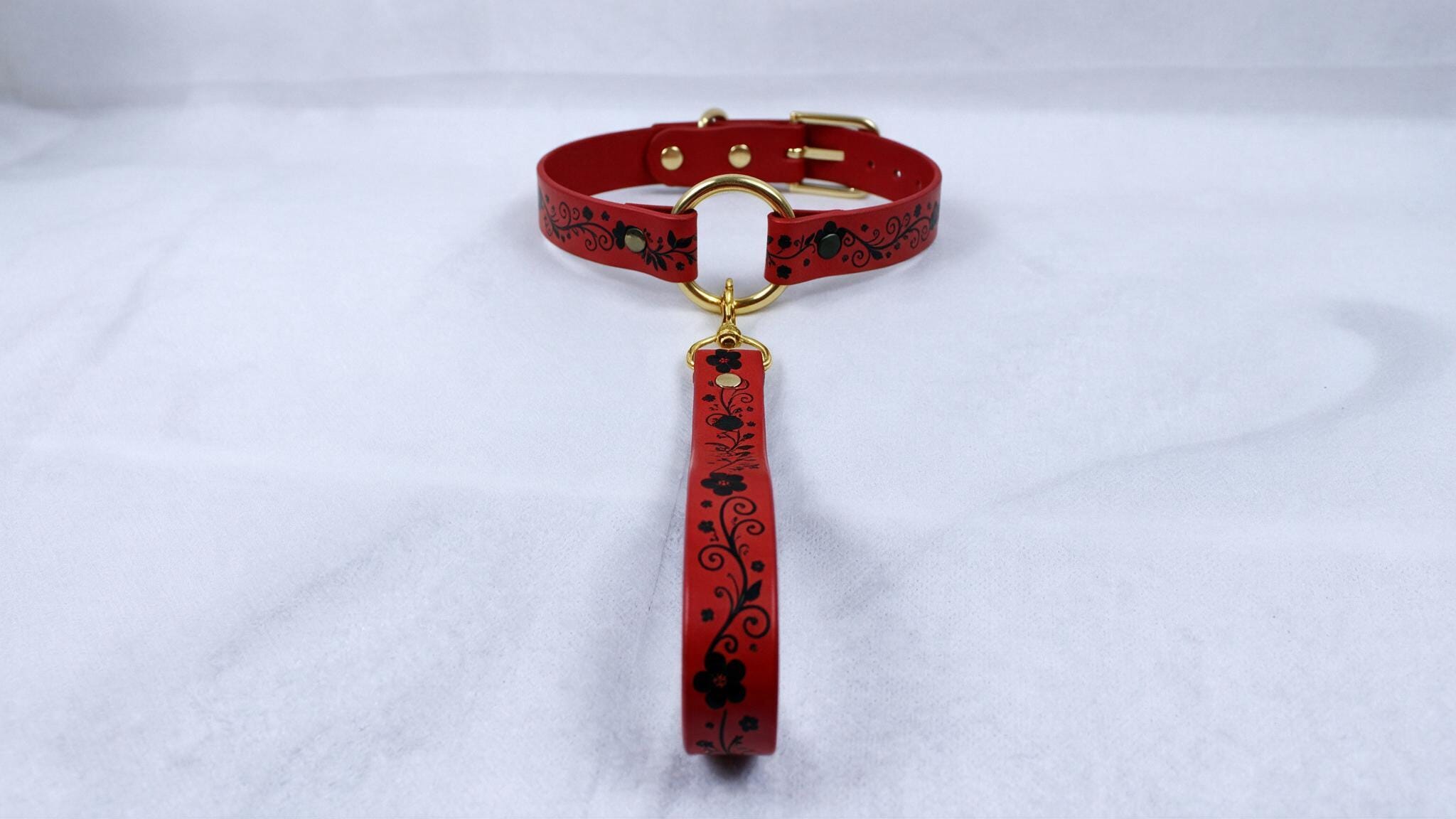 A red collar with a gold buckle and a red leash attached to it, placed on a white surface.