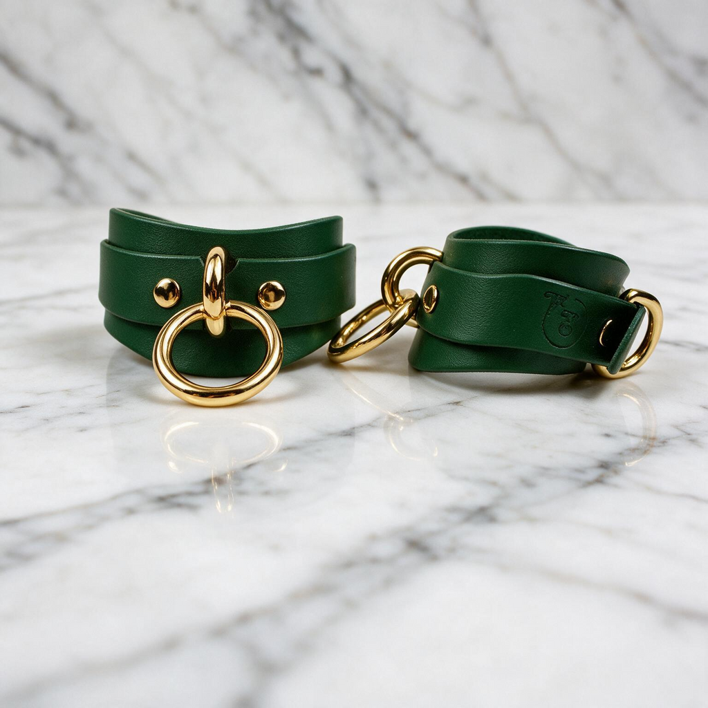 A pair of green leather straps with gold-colored metal rings and buckles, placed on a marble surface.