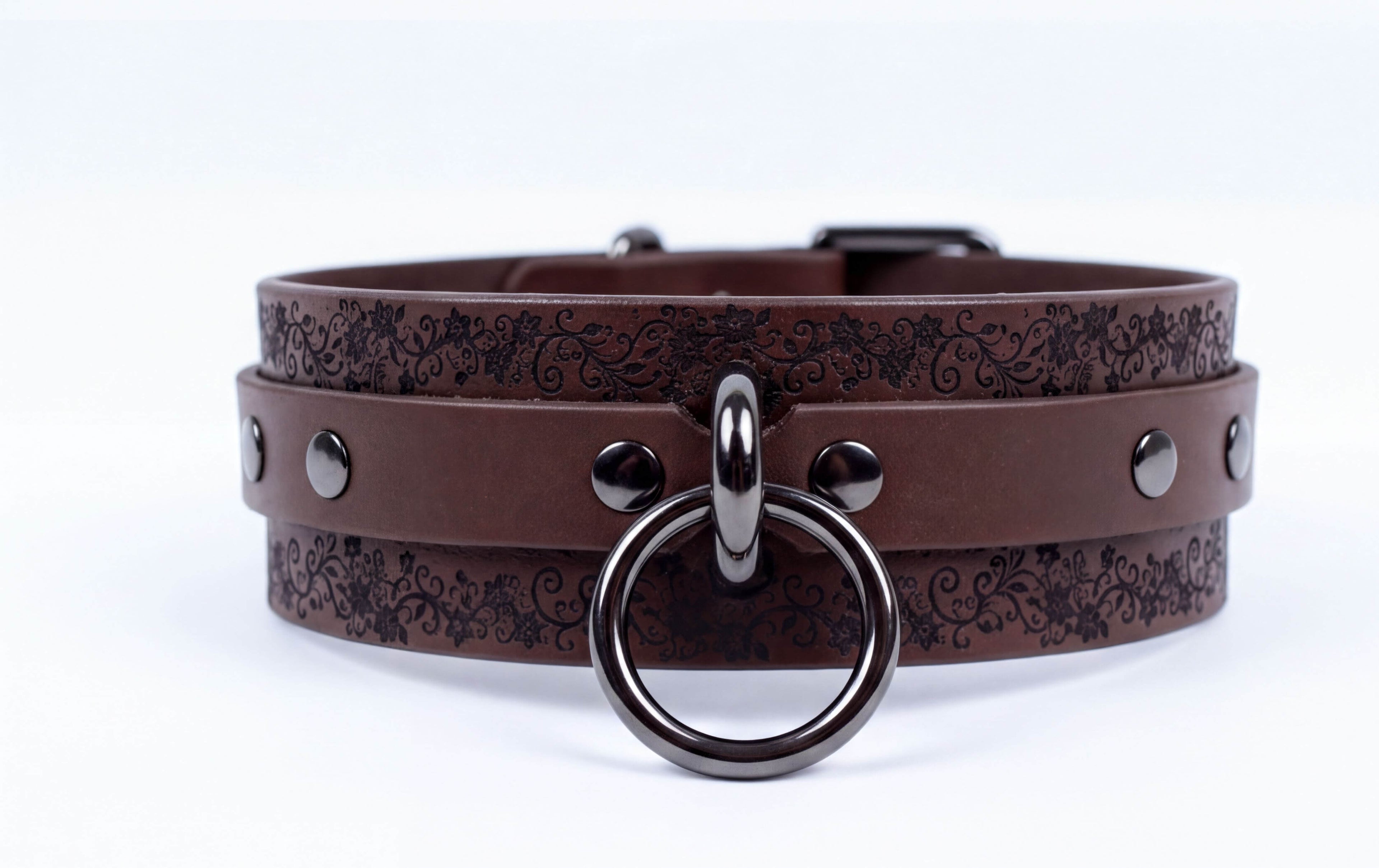 A brown leather choker collar with a metal ring and studs, featuring a floral pattern on the straps.