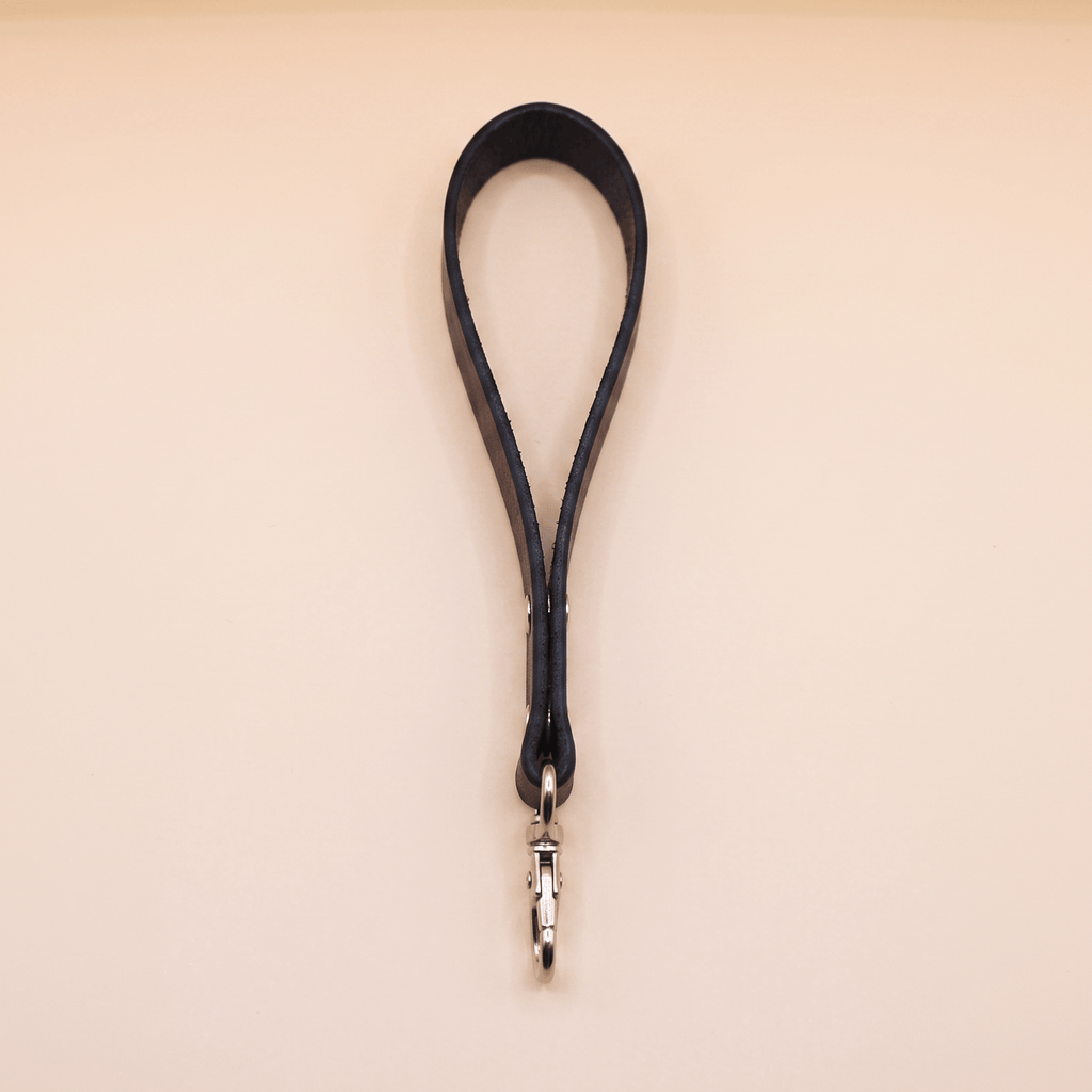 A black leather strap with a metal clasp attached to it, hanging against a light-colored background.