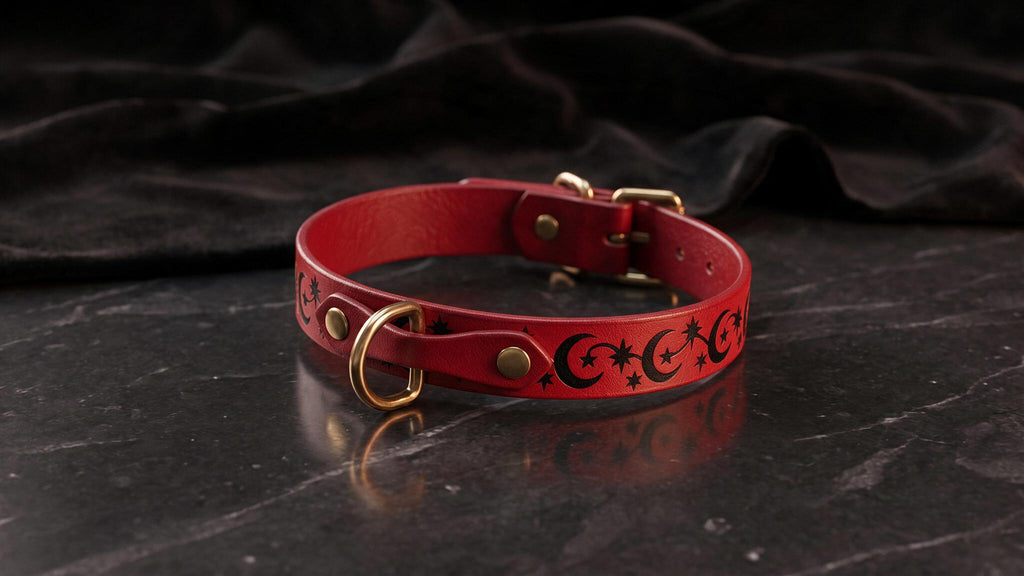 A red leather collar with a moon and star design on it, resting on a black marble surface.