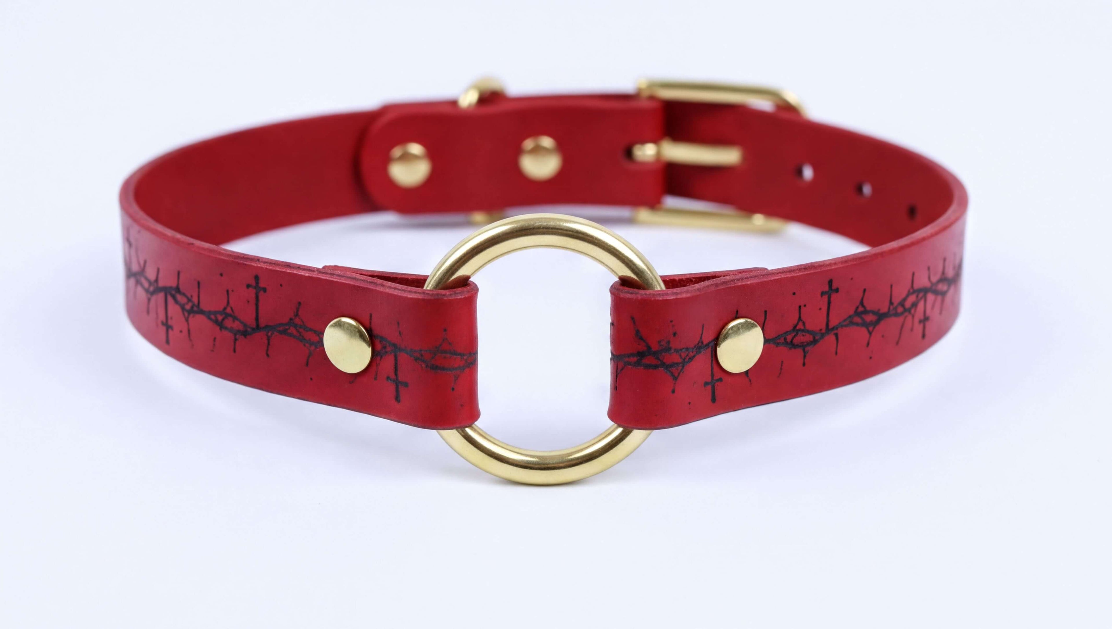 A red leather choker collar with a gold-colored metal ring and a black design on the front.