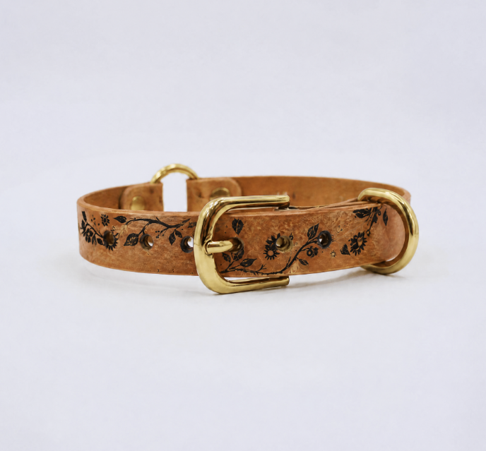 A tan leather dog collar with a floral pattern and two brass buckles.