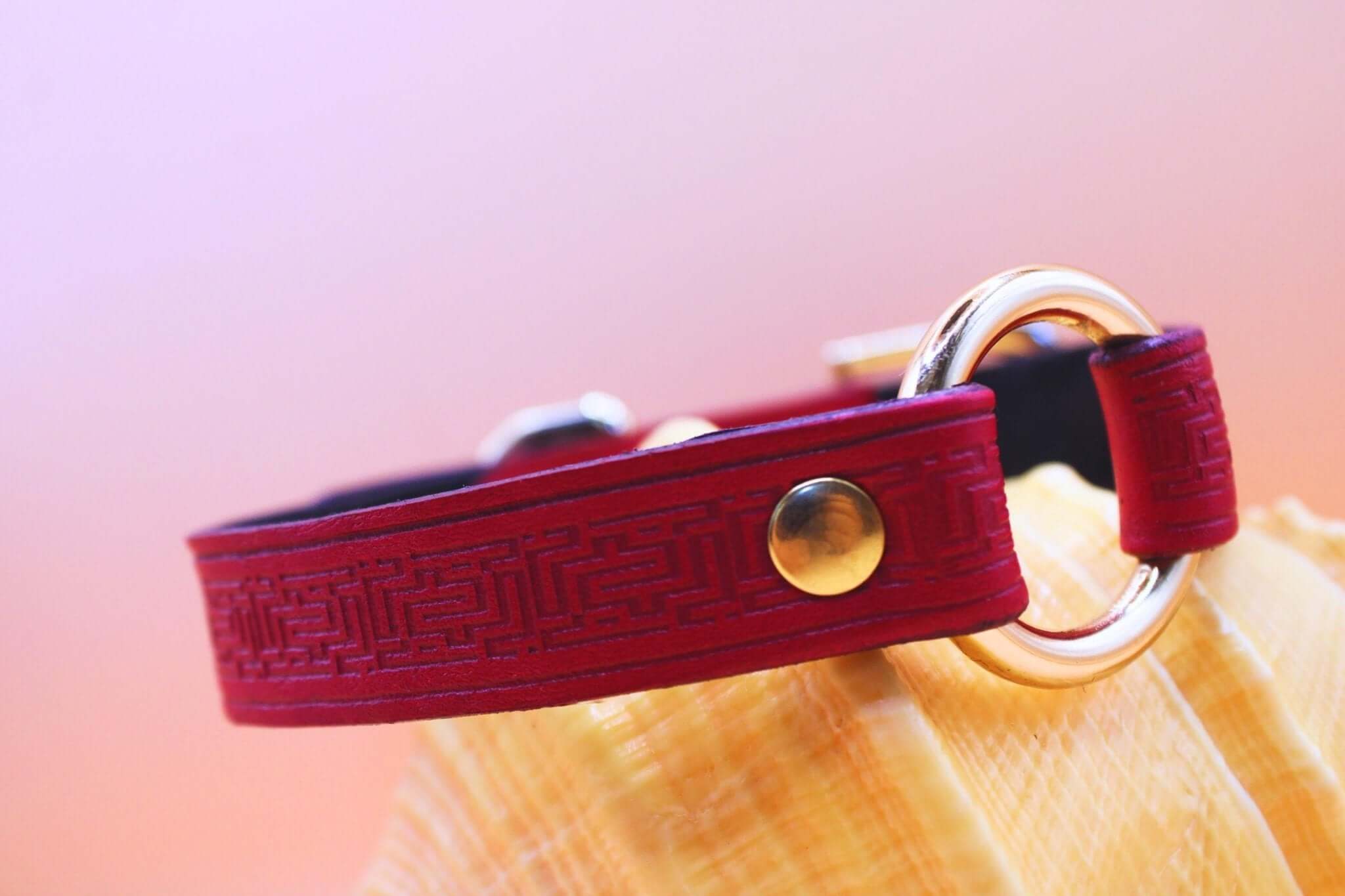 Deep red leather sub collar with gold O-ring, adorned with embossed labyrinth pattern, perfect for BDSM jewelry.
