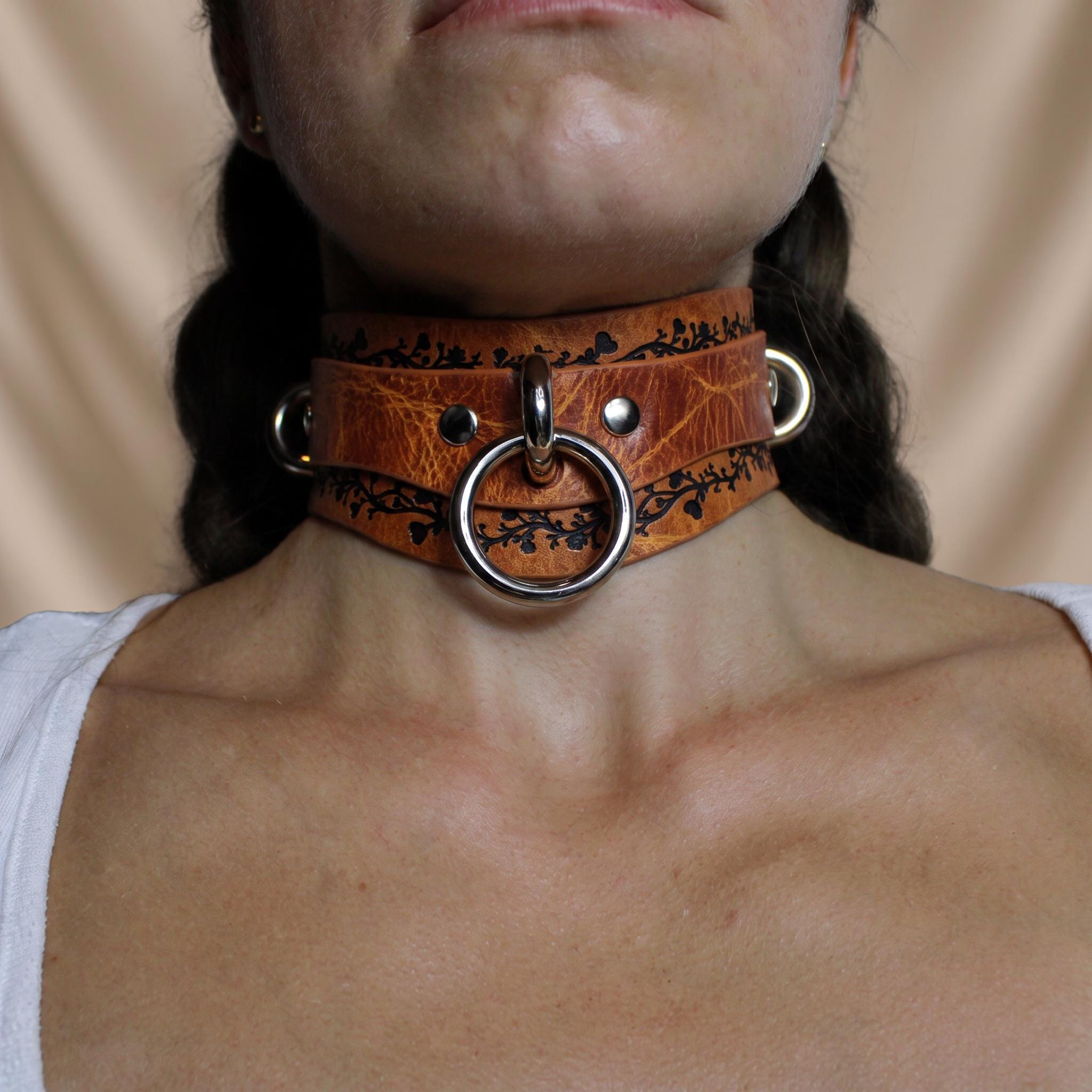 A close-up of a person wearing a leather choker necklace with metal rings and a metal ring on the front.