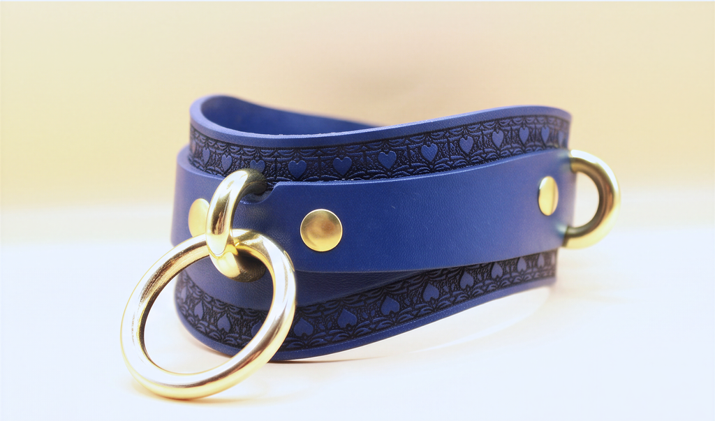 A blue leather choker necklace with a gold ring and two gold-colored metal rings on either side.