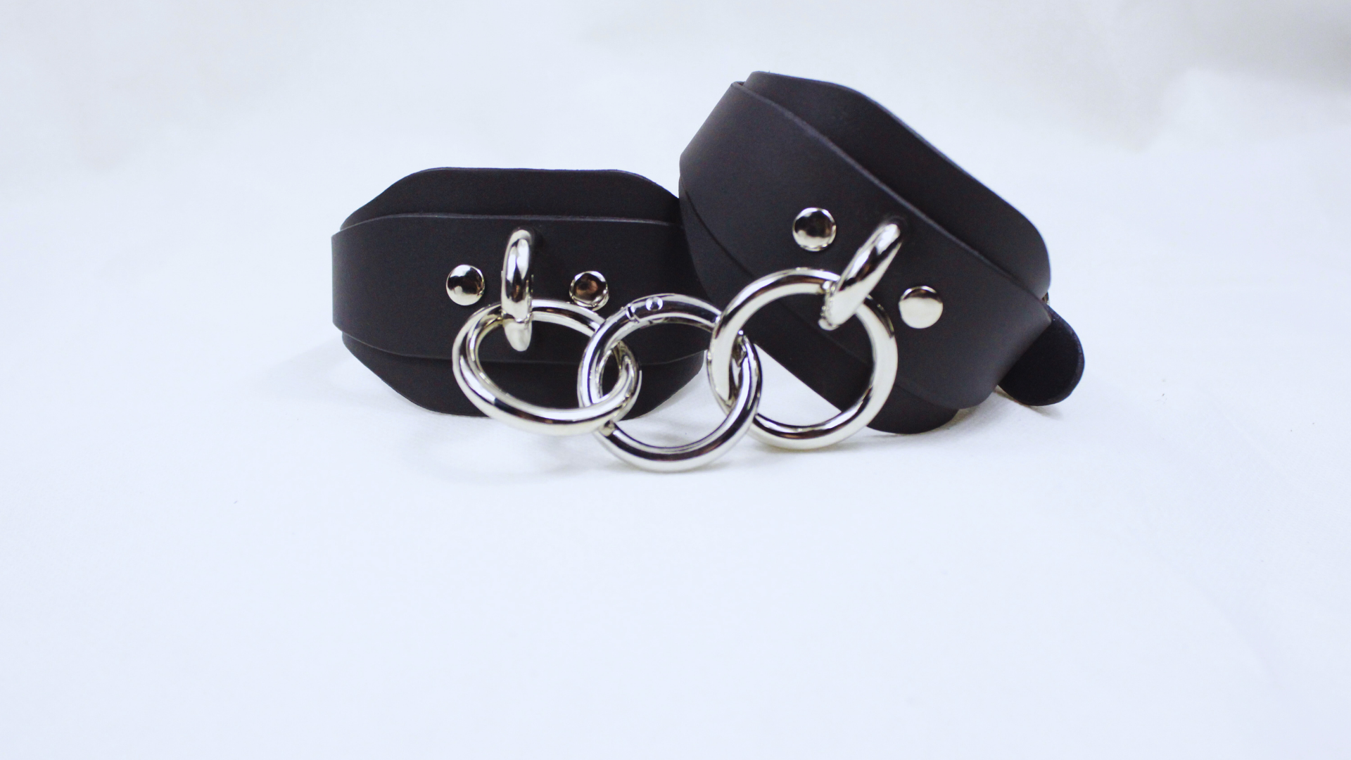 A pair of black leather straps with silver metal rings, arranged in a way that they appear to be connected by a loop.