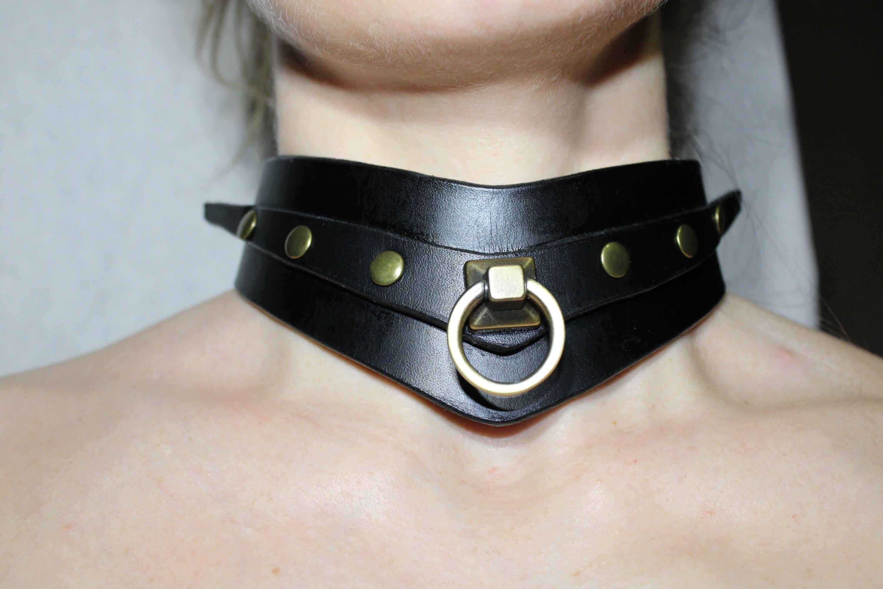 A close-up of a person's neck wearing a black leather choker necklace with a metal ring and studs.