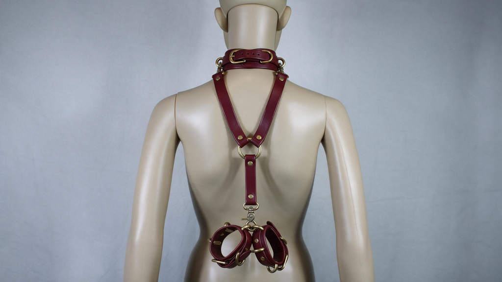 A mannequin wearing a burgundy leather harness with multiple straps and buckles, including a collar and a waist belt.