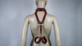 A mannequin wearing a burgundy leather harness with multiple straps and buckles, including a collar and a waist belt.