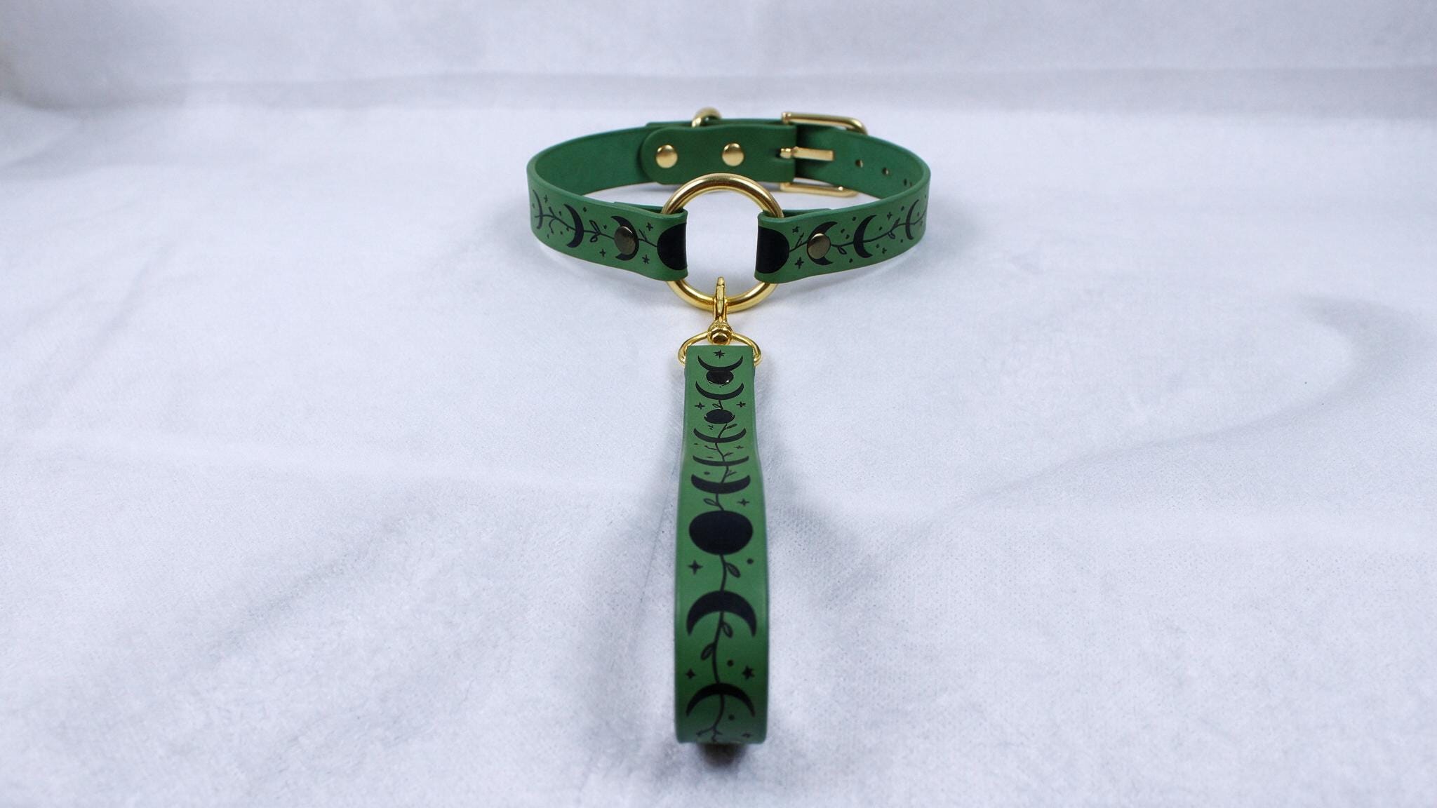 A green collar with a gold buckle and a black and white pattern on the strap is displayed against a white background.