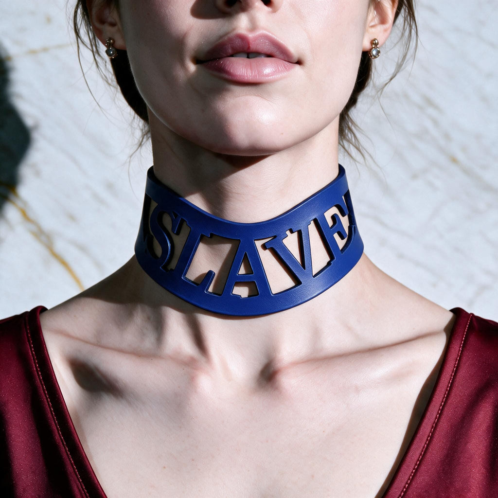 A close-up of a woman wearing a blue choker necklace with the word "SLAVE" cut out in the shape of the word.