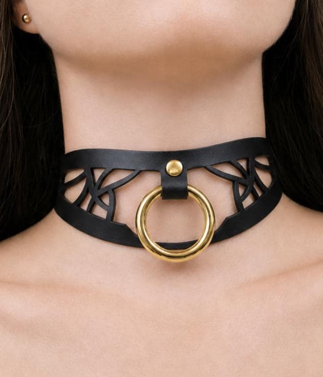 A close-up view of a woman's neck and chest area wearing a black choker necklace with a gold ring.