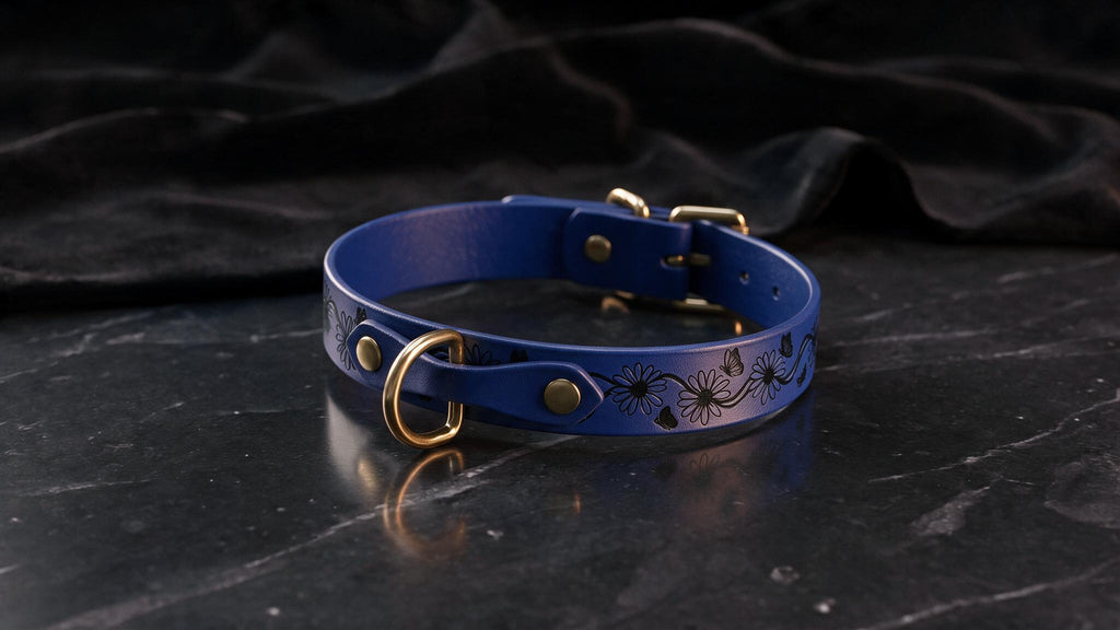 A blue leather collar with a floral design and a gold-colored buckle is displayed on a black marble surface.