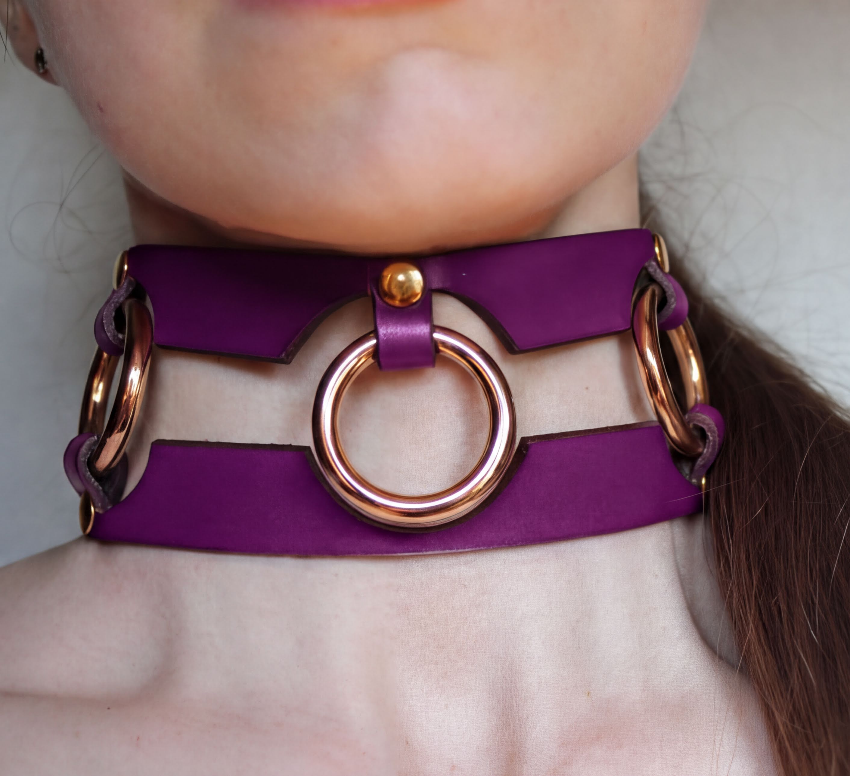 A close-up of a person's neck wearing a purple leather choker necklace with gold-colored rings.
