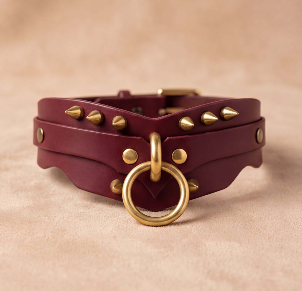 A burgundy leather choker necklace with gold studs and a gold ring, displayed on a beige background.