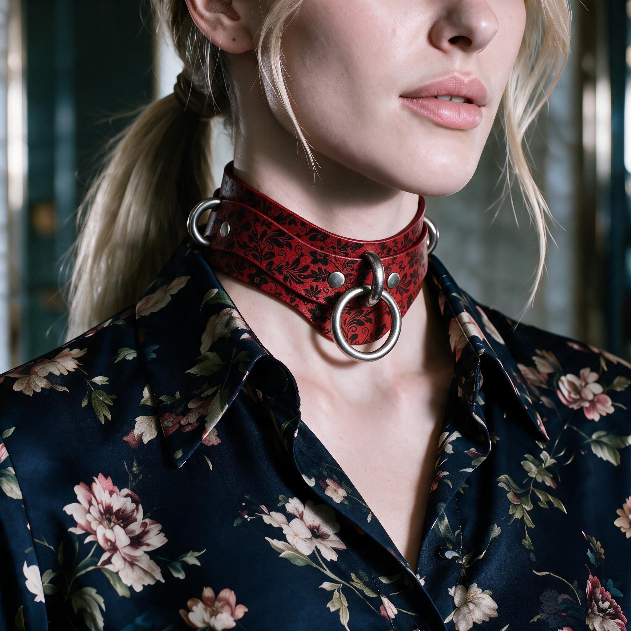 A close-up of a woman wearing a red choker necklace with a floral pattern, paired with a dark blue floral blouse.