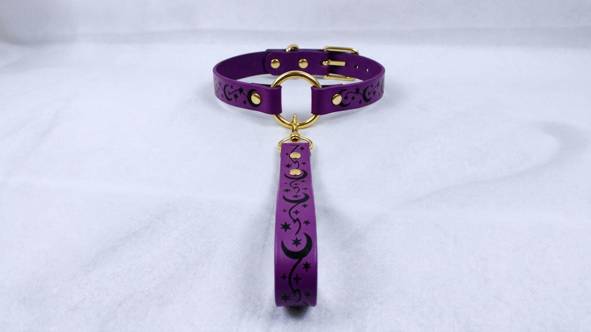 A purple collar with a gold buckle and a black star-and-crescent design on the strap is displayed against a white background.