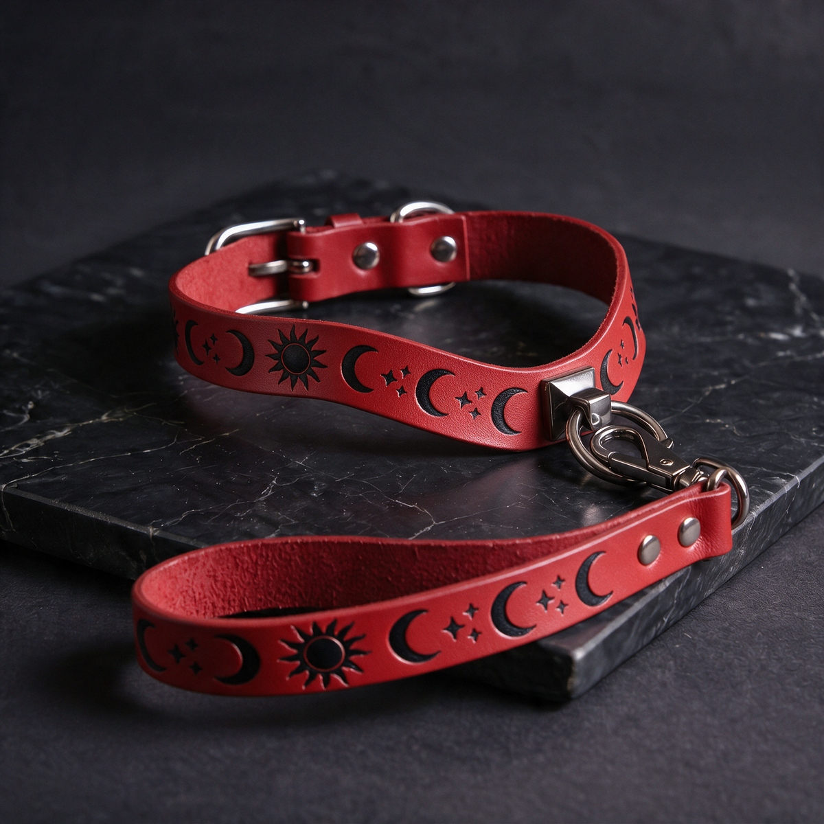 A red leather collar with a metal buckle and a matching red leather leash with a metal hook attached, both resting on a black marble surface.