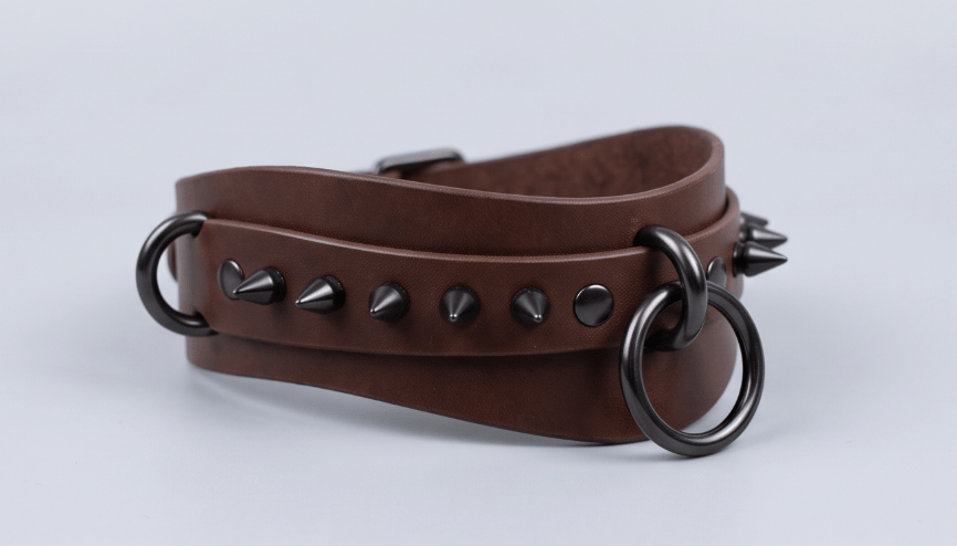 A brown leather choker necklace with metal spikes and circular metal rings.