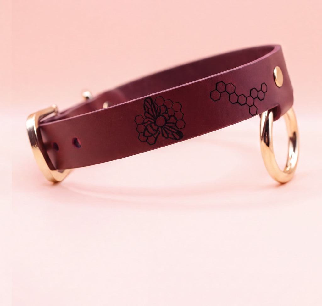 A burgundy leather dog collar with a floral design and two gold-colored rings on the sides.