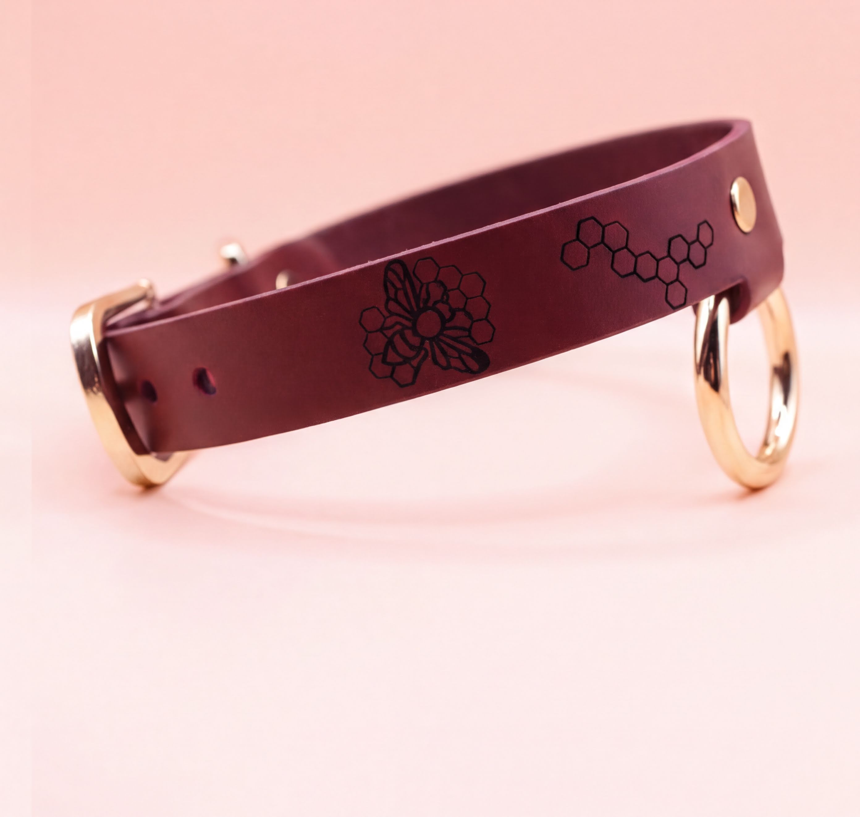 A burgundy leather dog collar with a floral design and two gold-colored rings on the sides.