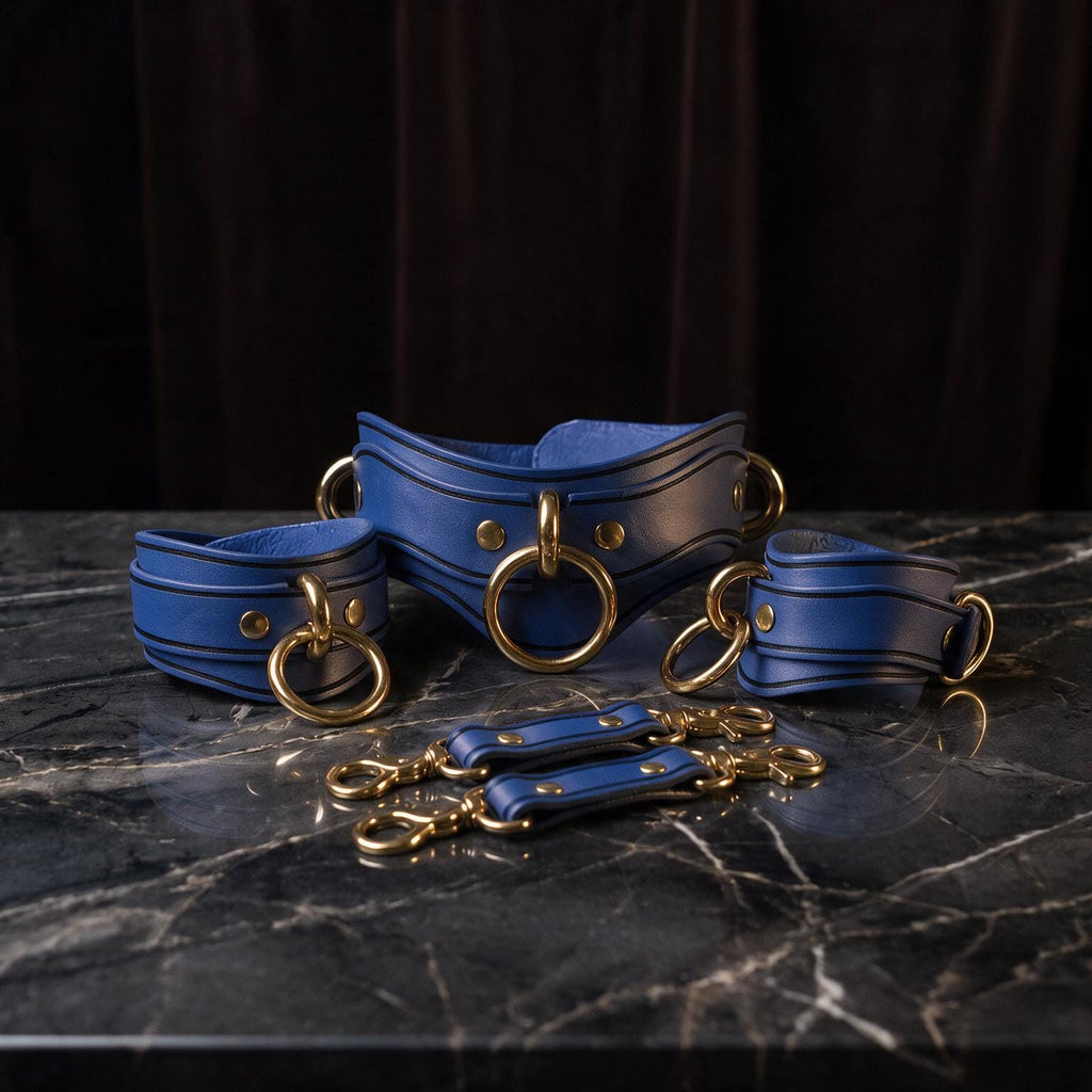 A set of blue leather choker necklaces with gold-colored metal rings, arranged on a marble surface.