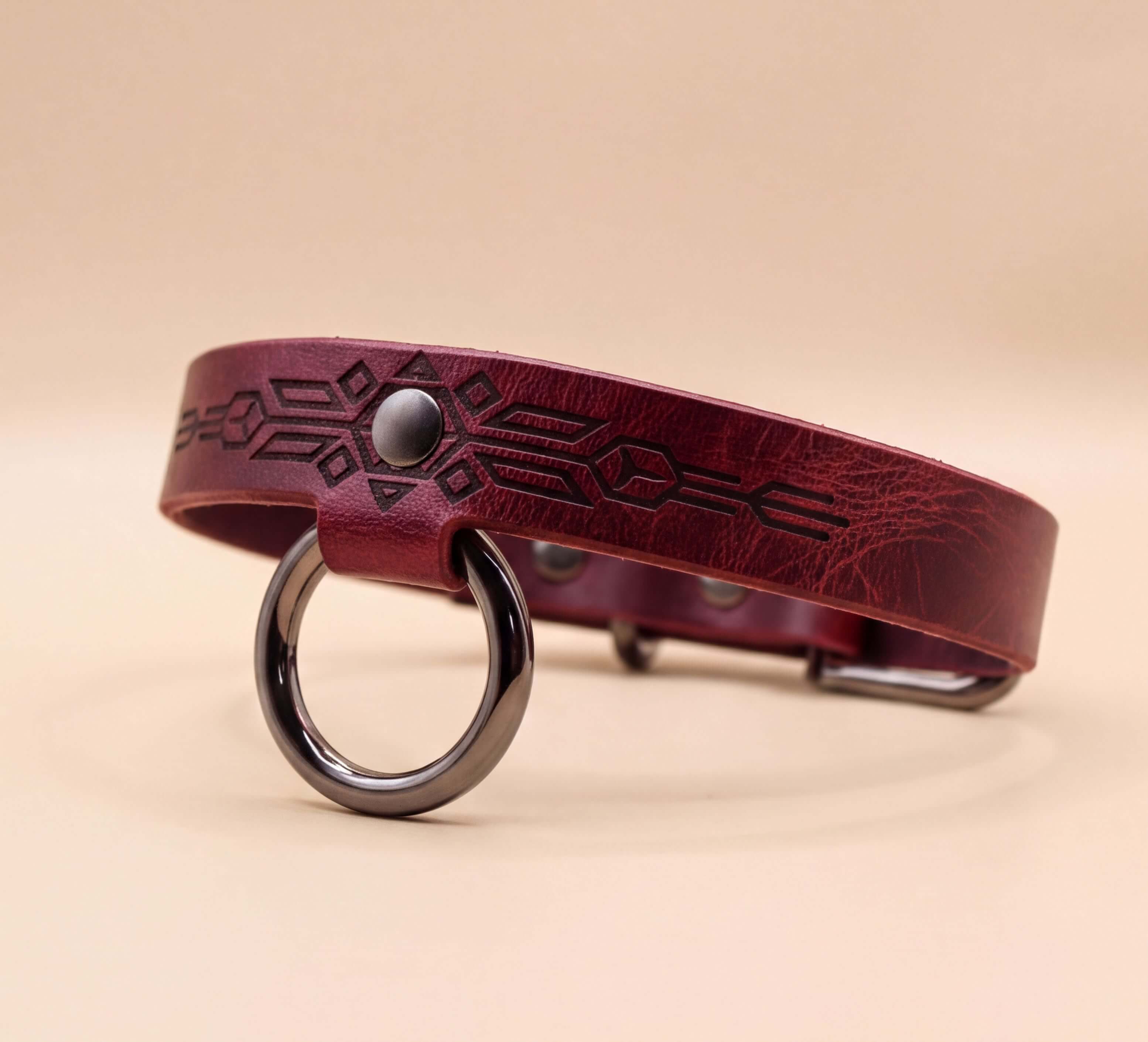 A burgundy leather dog collar with a metal ring and a geometric pattern design.