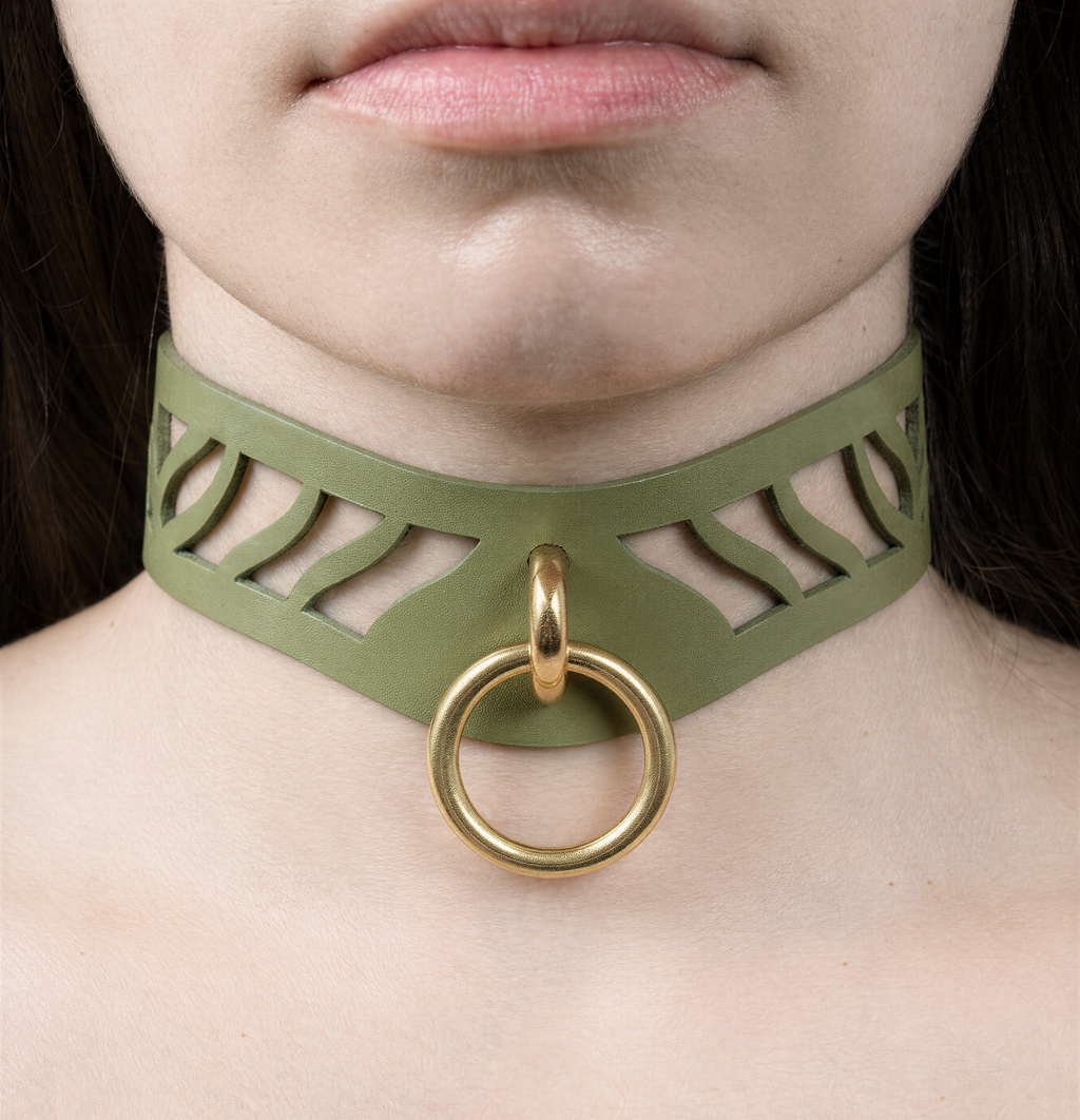 A close-up of a person's neck and chest area, featuring a green choker necklace with a gold ring and a cutout design.