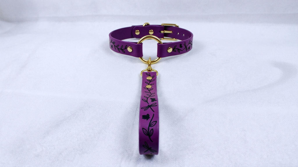 A purple collar with a gold-colored buckle and a floral pattern on the strap is displayed against a white background.