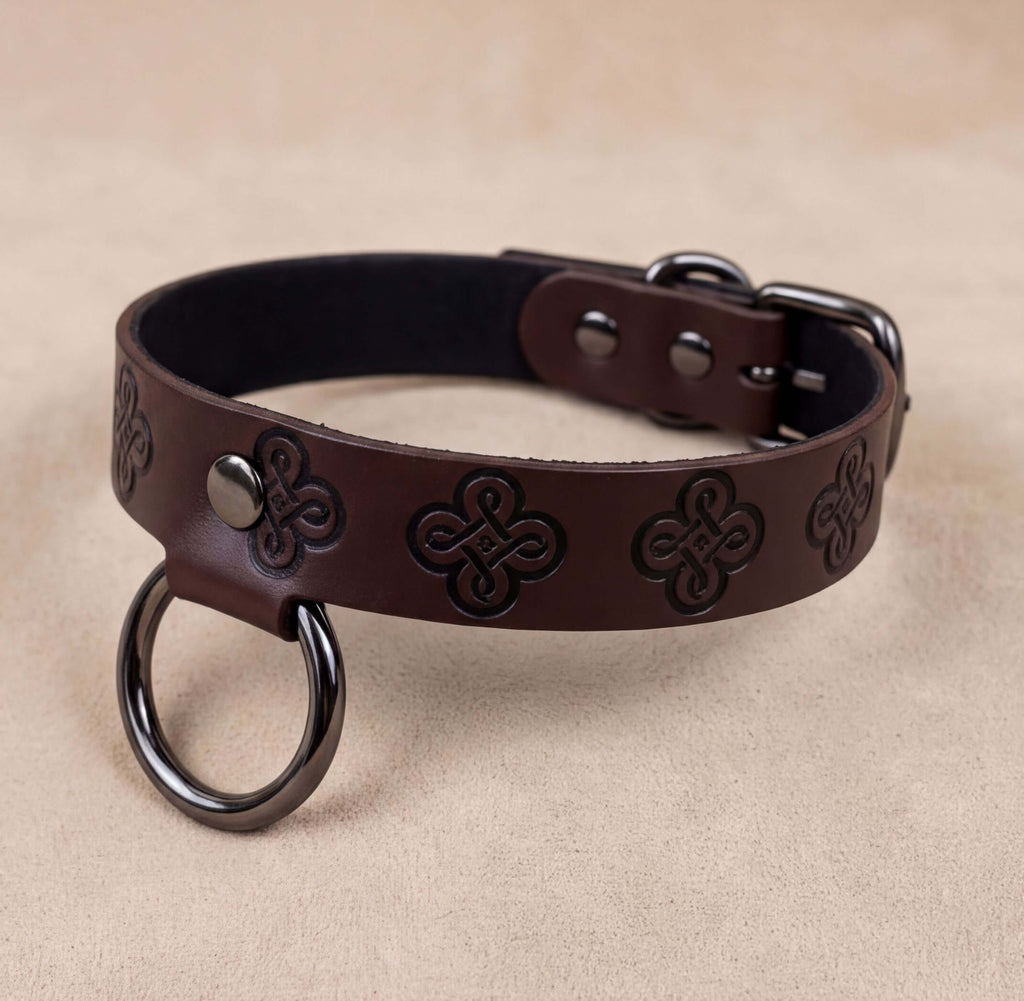 A brown leather dog collar with a metal ring and decorative patterns.