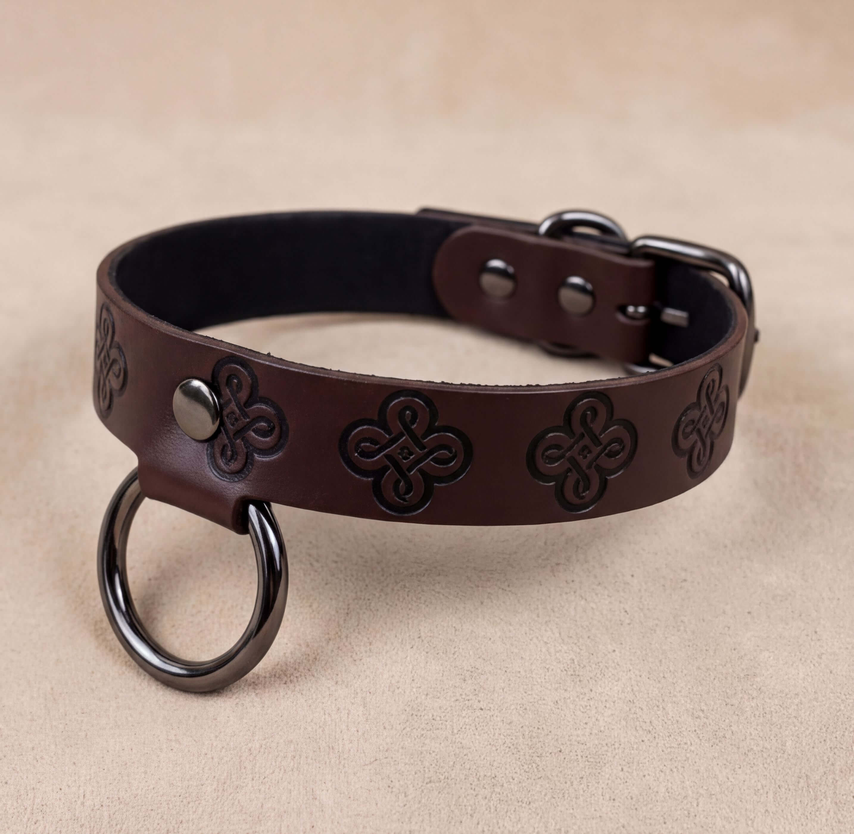 A brown leather dog collar with a metal ring and decorative patterns.
