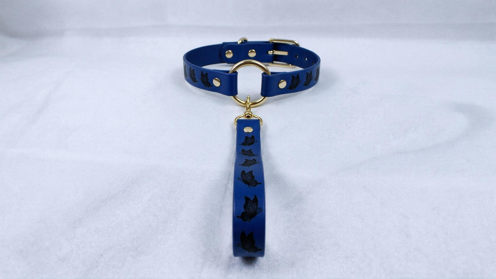 A blue collar with a gold buckle and a black cat design on it, placed on a white surface.