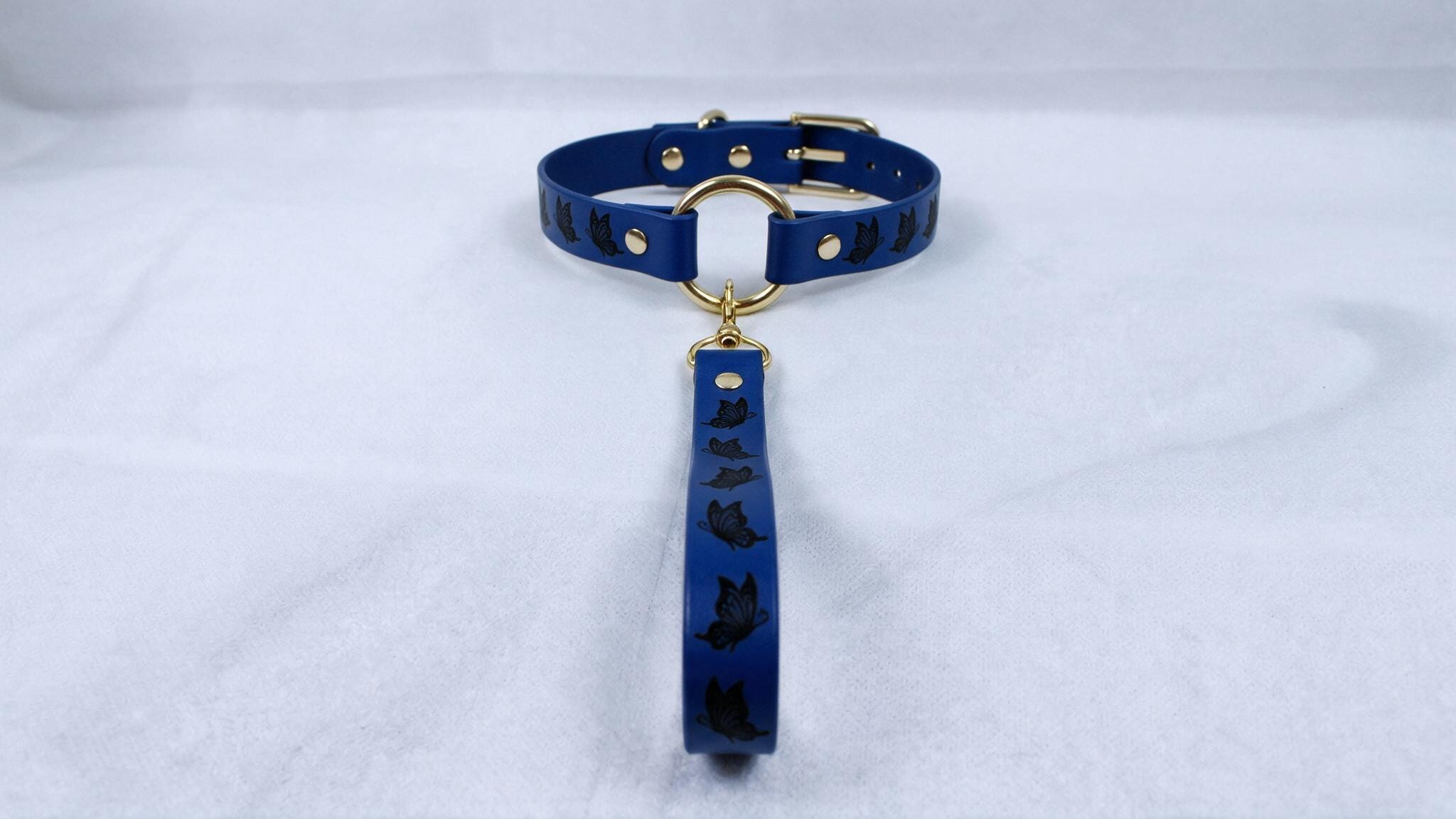 A blue collar with a gold buckle and a black cat design on it, placed on a white surface.