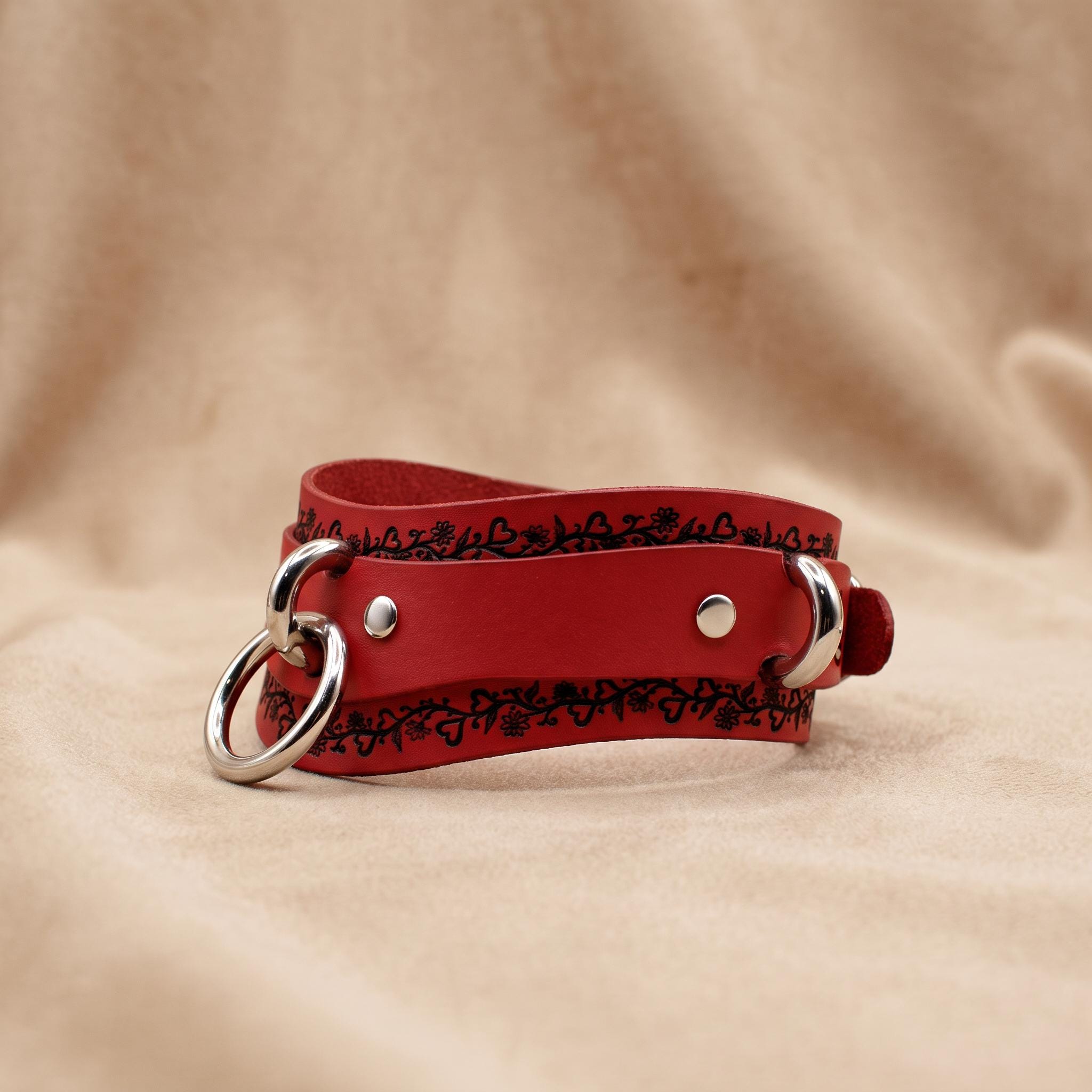 A red leather choker necklace with a metal ring and decorative elements on the clasp.