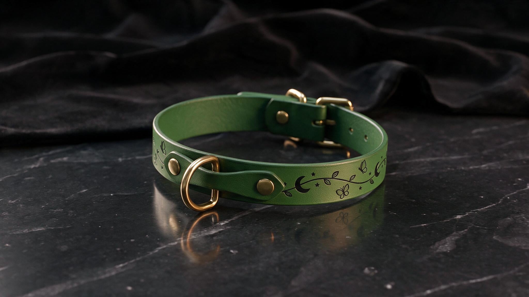 A green leather collar with a floral design and a gold-colored buckle is displayed on a black marble surface.
