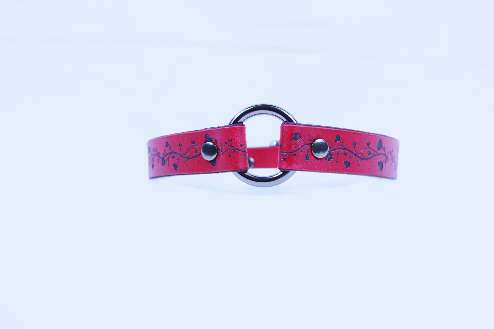 A red leather choker necklace with a metal ring and decorative elements.