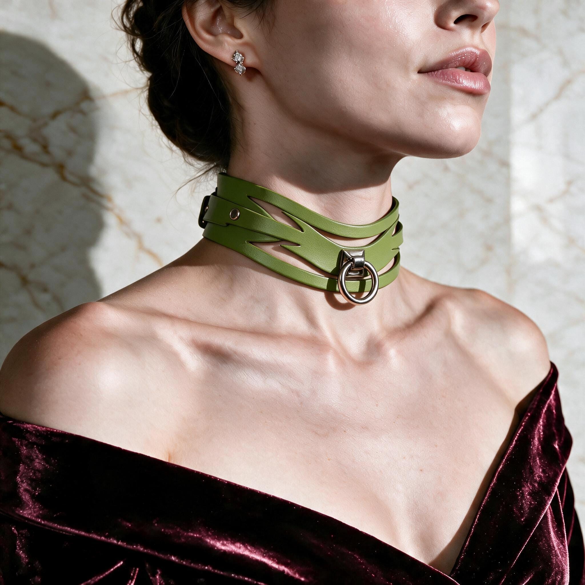 A woman wearing a green choker necklace with a metal buckle, posing against a marble wall.