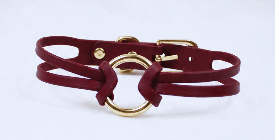 A burgundy leather choker necklace with a gold-colored circular buckle.
