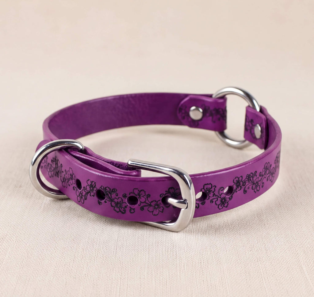A purple leather dog collar with a floral pattern and metal rings.