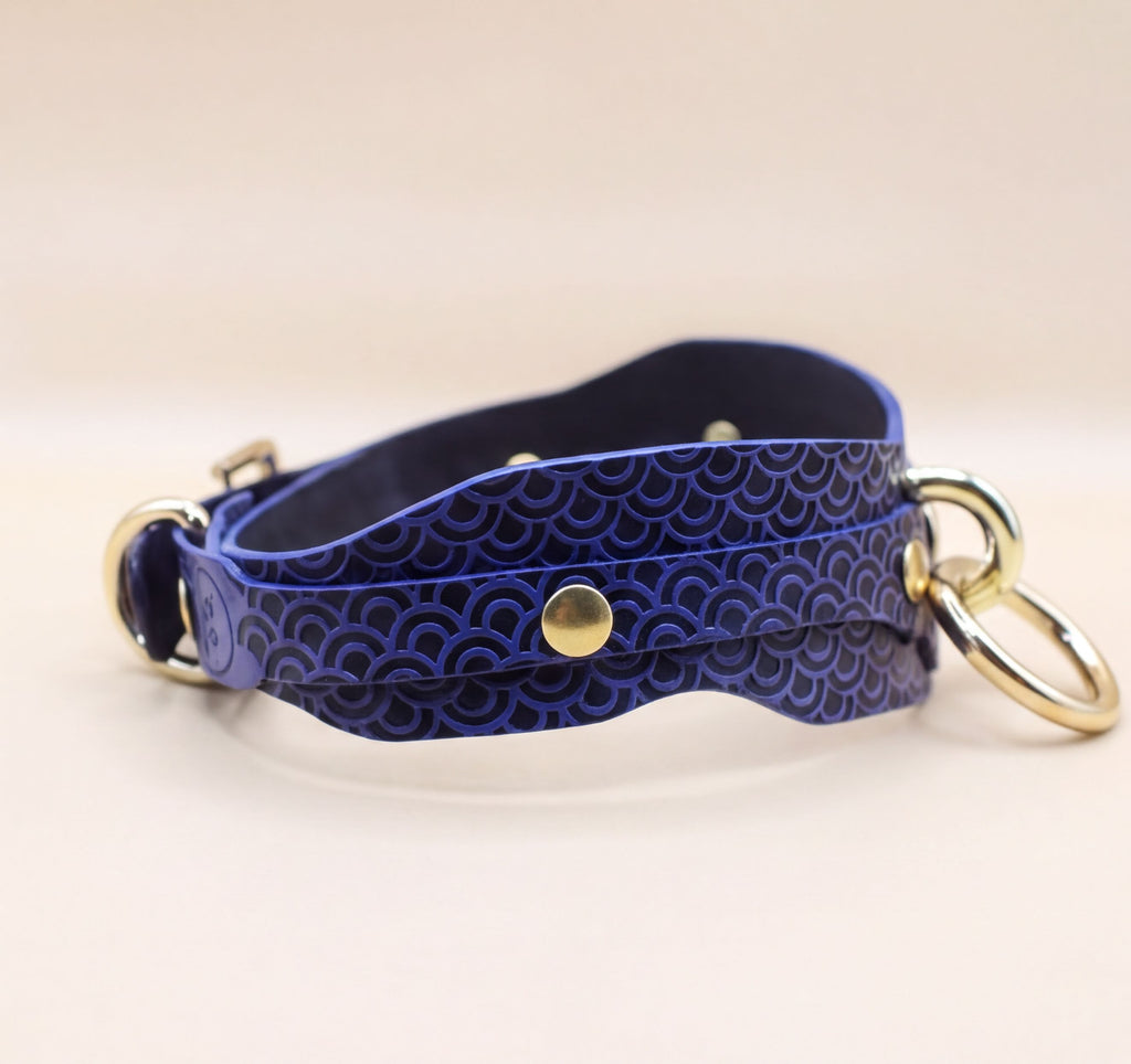 A blue leather strap with a patterned design, featuring a gold buckle and two metal rings.