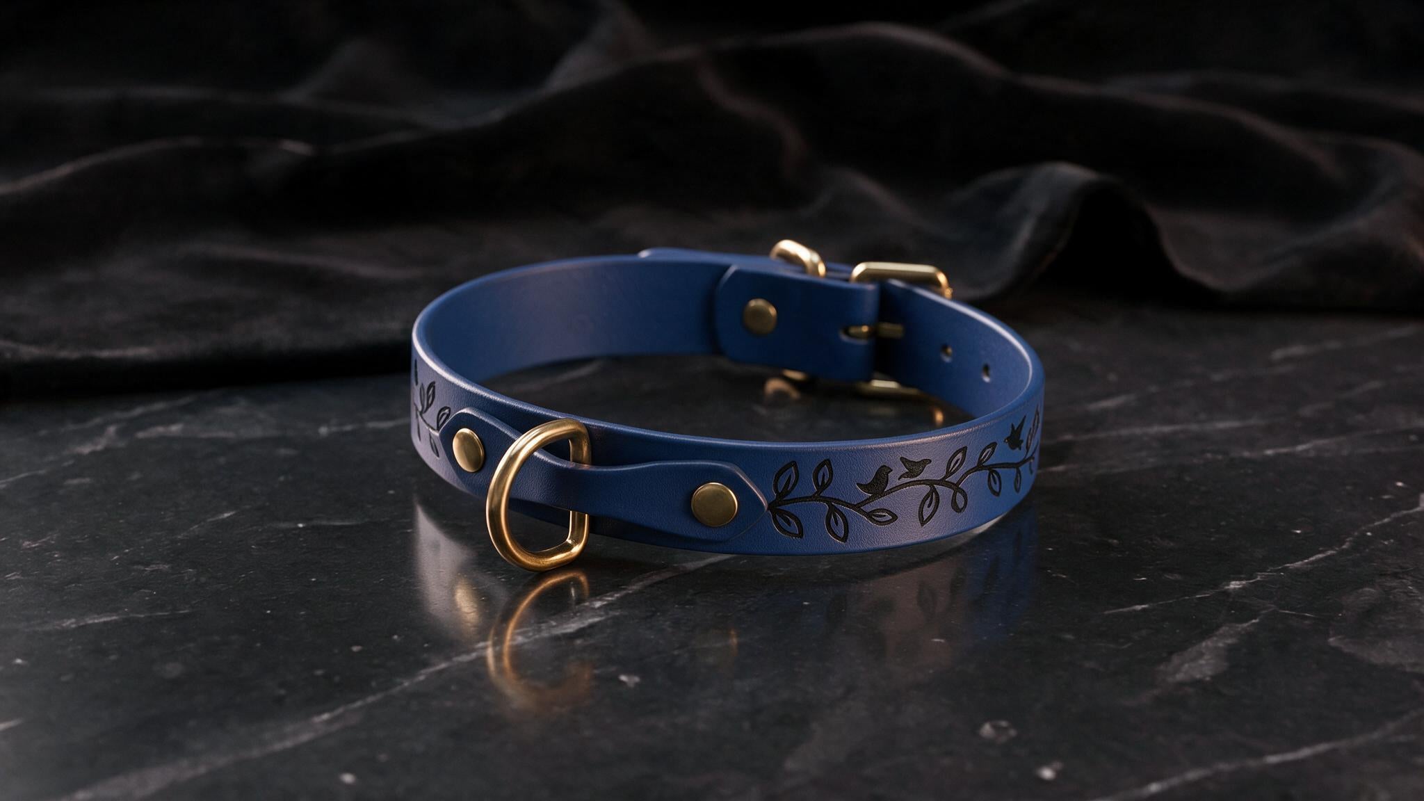 A blue leather collar with a leaf design sits on a black marble surface.