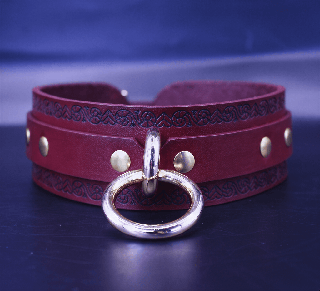 A burgundy leather choker necklace with a gold-colored metal ring and decorative elements on the band.